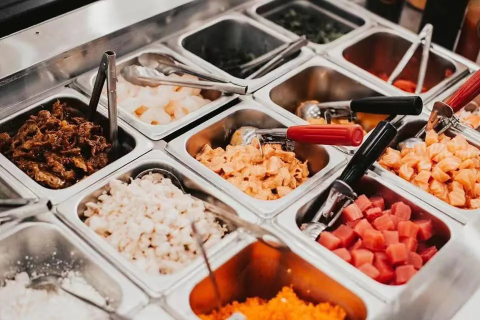 Poke bar with metal trays of fresh ingredients like marinated fish, shrimp, and toppings at Natural Kitchen Wilton, a Fast Casual Restaurant in Wilton
