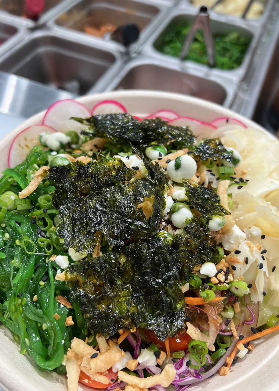 Poke bowl topped with seaweed, green seaweed salad, radish slices, and crispy bits at Natural Kitchen Wilton, a Fast Casual Restaurant in Wilton